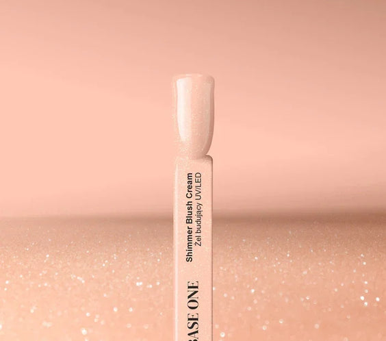 Cured nail tip displaying the warm beige Base One Shimmer Blush Cream builder gel (15g), featuring subtle, embedded shimmering particles.