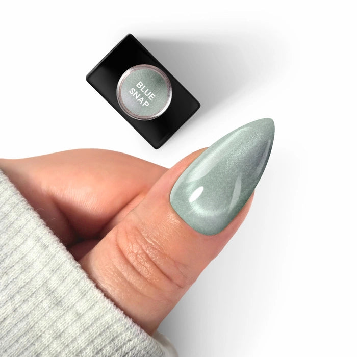 Close-up of a manicured almond-shaped nail featuring Silcare maniMORE Cat Eye Blue Snap gel polish, displaying a multidimensional teal shimmer next to the product bottle.