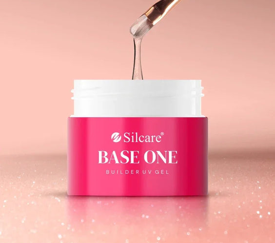 A brush lifting thick, shimmering pink Silcare Base One Builder UV Gel in Vanillia Rose from a pink and white jar, set against a sparkling rose gold background.
