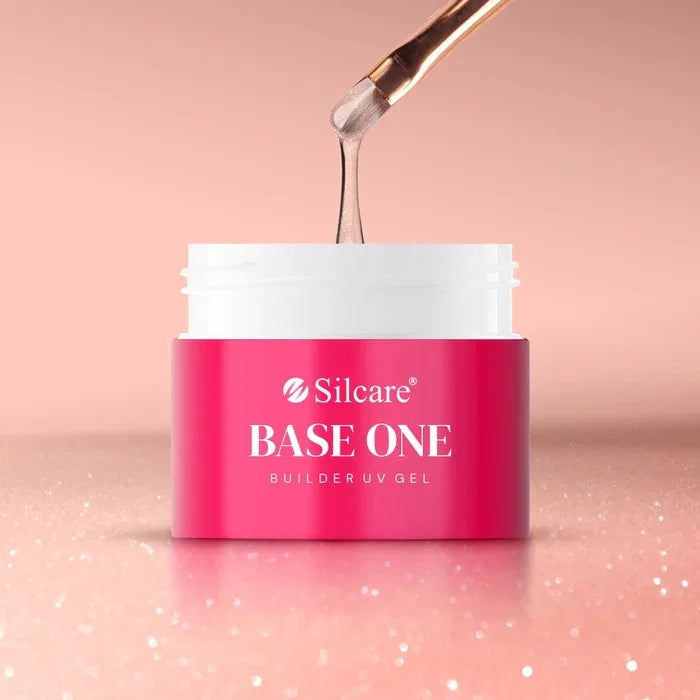 A brush lifting thick, shimmering pink Silcare Base One Builder UV Gel in Vanillia Rose from a pink and white jar, set against a sparkling rose gold background.