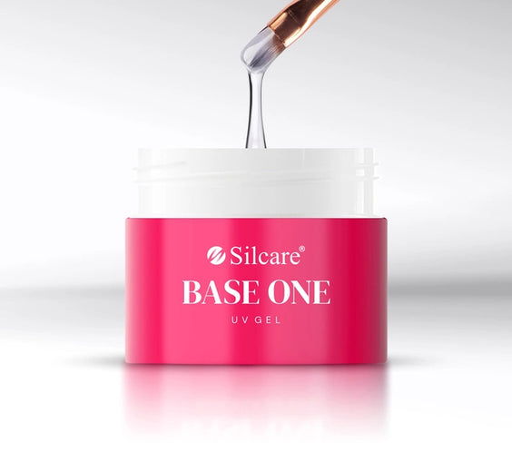 A close-up view of a brush applying medium-thick, white UV builder gel from a pink Base One French White Opal jar by Silcare.
