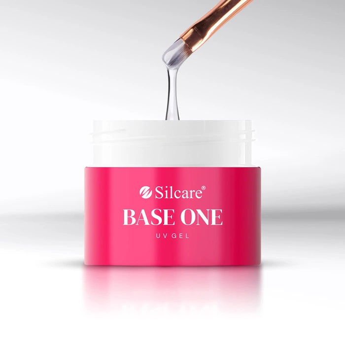 A close-up view of a brush applying medium-thick, white UV builder gel from a pink Base One French White Opal jar by Silcare.