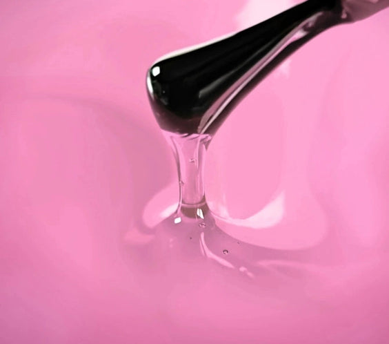 Brush applying semi-transparent pink gel top coat with glass effect texture on pink background