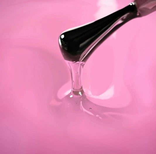 Brush applying semi-transparent pink gel top coat with glass effect texture on pink background