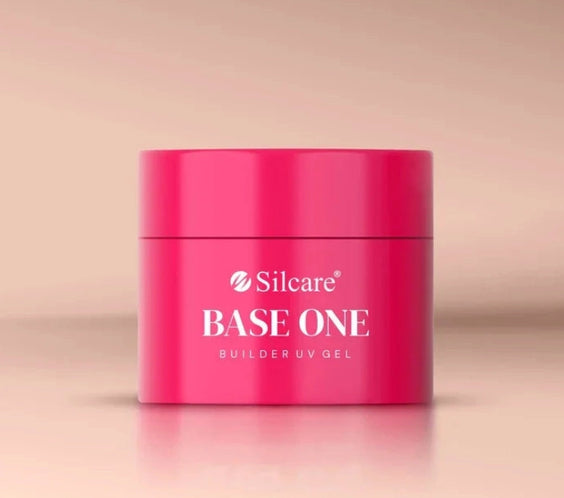 Front view of the Silcare Base One Builder UV Gel jar in bright pink packaging with the Silcare logo and "BASE ONE Builder UV Gel" printed on the container. The closed gel jar is photographed against a soft beige background, showcasing the professional nail builder gel packaging used for nail extensions, overlays, and salon manicures.