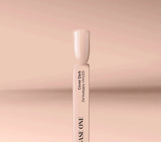 Close-up of the Silcare Base One Cover Dark builder UV/LED gel colour swatch stick featuring a glossy nude beige shade. The swatch displays the product name "Cover Dark" on a white sample stick against a soft beige background, illustrating the natural camouflage colour for nail extensions, overlays, nail bed enhancement, and professional salon manicures.