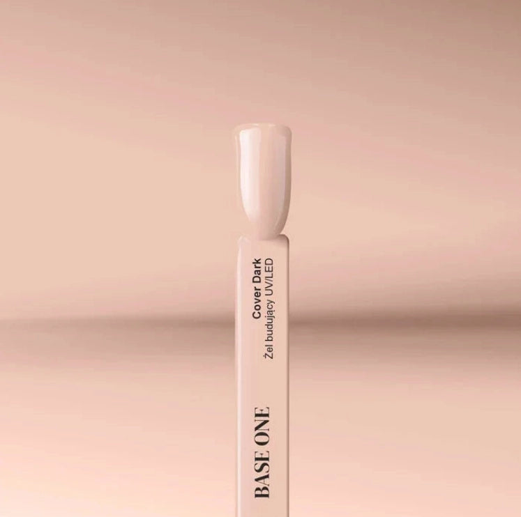 Close-up of the Silcare Base One Cover Dark builder UV/LED gel colour swatch stick featuring a glossy nude beige shade. The swatch displays the product name "Cover Dark" on a white sample stick against a soft beige background, illustrating the natural camouflage colour for nail extensions, overlays, nail bed enhancement, and professional salon manicures.
