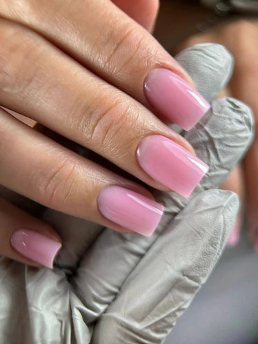 Close-up of glossy square-shaped nails finished with Silcare Brush One Sassy Flirt BIAB Builder Gel in a soft candy pink shade. Elegant salon manicure with a smooth self-levelling finish, ideal for natural nail strengthening, overlays, short extensions and long-lasting professional results.
